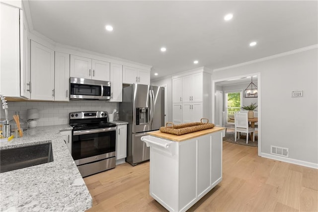 kitchen featuring appliances with stainless steel finishes, crown molding, tasteful backsplash, white cabinets, and a sink