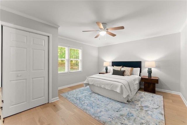 bedroom featuring crown molding, baseboards, light wood-type flooring, a ceiling fan, and a closet