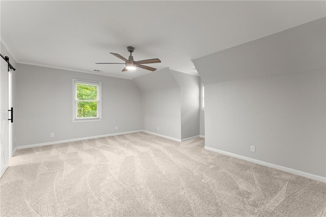 additional living space with a ceiling fan, light carpet, baseboards, and a barn door