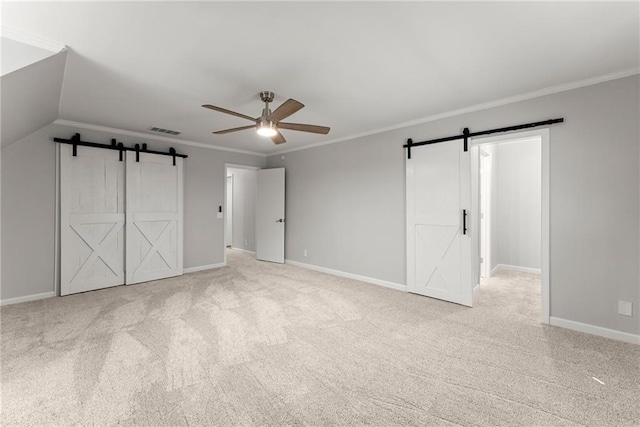 unfurnished bedroom featuring a barn door, carpet floors, baseboards, and ornamental molding
