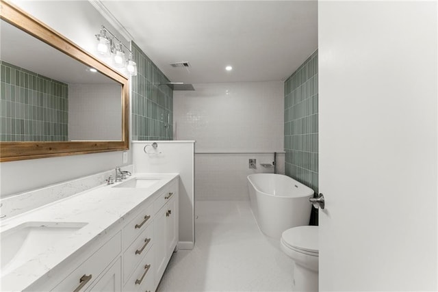 bathroom featuring tile walls, a freestanding tub, walk in shower, double vanity, and recessed lighting