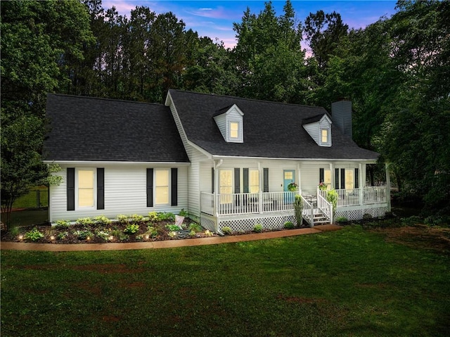 cape cod house featuring covered porch, a chimney, a front lawn, and a shingled roof