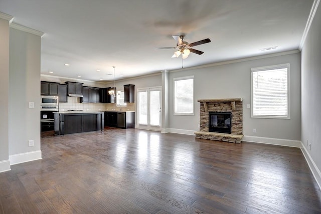 unfurnished living room with ceiling fan, dark hardwood / wood-style flooring, a stone fireplace, and crown molding