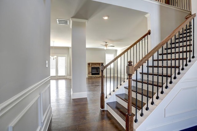 stairs with hardwood / wood-style floors, ceiling fan with notable chandelier, a stone fireplace, and crown molding