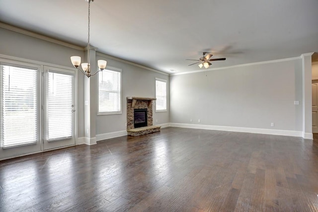 unfurnished living room featuring a stone fireplace, crown molding, dark hardwood / wood-style flooring, and ceiling fan with notable chandelier