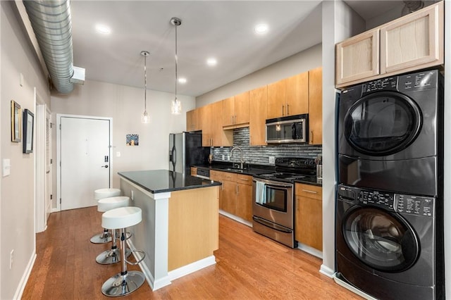 kitchen featuring stacked washer / dryer, light wood-style floors, appliances with stainless steel finishes, a center island, and a kitchen bar