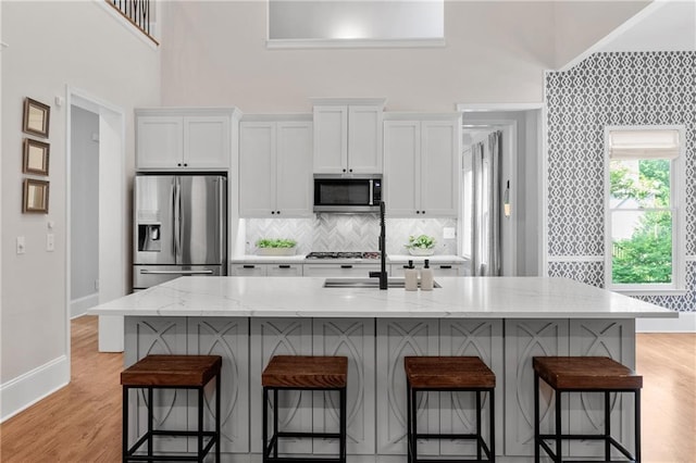 kitchen with white cabinets, appliances with stainless steel finishes, a sink, and a towering ceiling