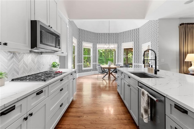kitchen featuring backsplash, appliances with stainless steel finishes, light stone countertops, a sink, and light wood finished floors