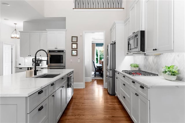 kitchen featuring decorative backsplash, wood finished floors, white cabinets, a sink, and stainless steel appliances