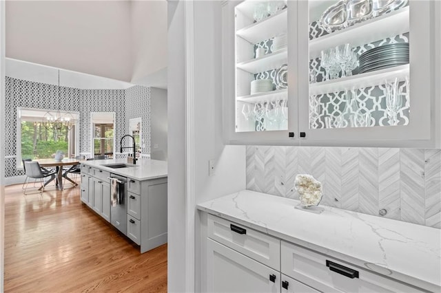 bar featuring stainless steel dishwasher, an inviting chandelier, wallpapered walls, a sink, and light wood-style flooring