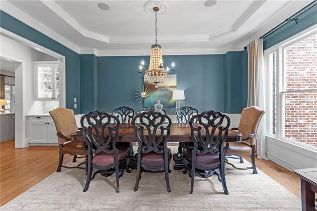 dining room with an inviting chandelier, a raised ceiling, and light wood-style floors