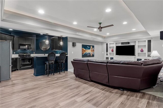 living room with light wood-style floors, a ceiling fan, crown molding, and a tray ceiling