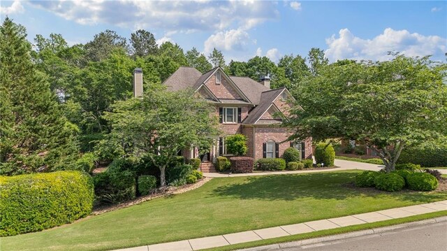 view of front of house featuring a chimney, a front lawn, and brick siding