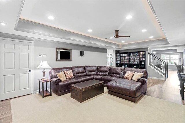 living room featuring a ceiling fan, crown molding, stairway, a raised ceiling, and light wood finished floors