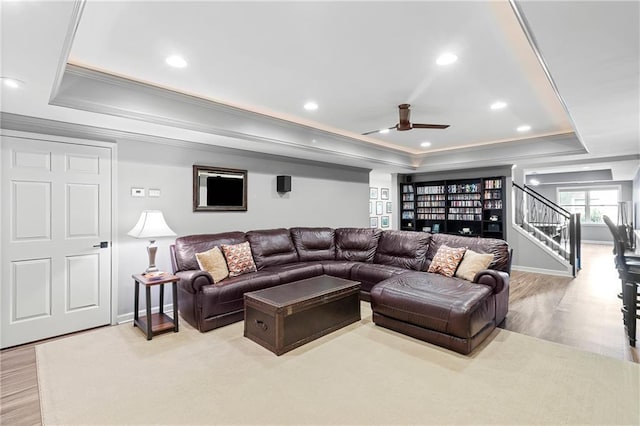 living room featuring a ceiling fan, crown molding, stairway, a raised ceiling, and light wood finished floors