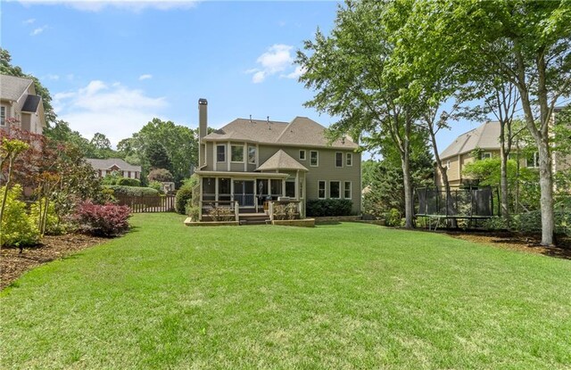rear view of property with fence, a chimney, a sunroom, a lawn, and a trampoline