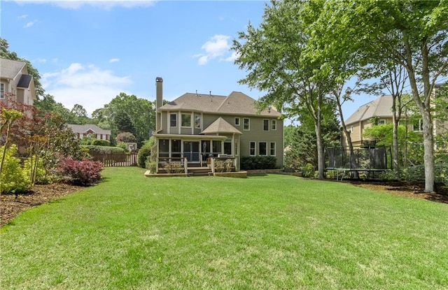 rear view of property with fence, a chimney, a sunroom, a lawn, and a trampoline
