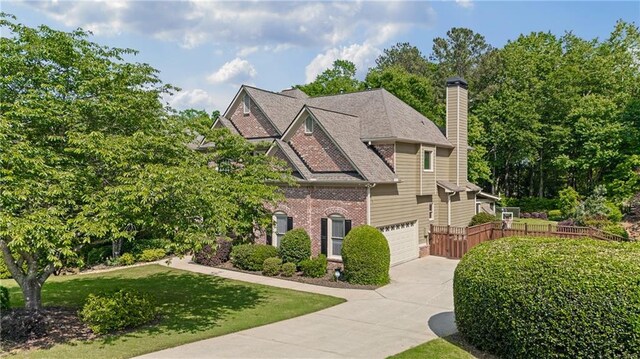 view of front of house with fence, an attached garage, brick siding, a chimney, and driveway