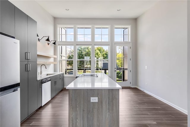 kitchen with gray cabinets, white appliances, a center island, and sink