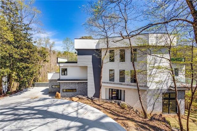 modern home featuring concrete driveway, stone siding, and stucco siding