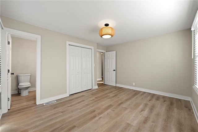 unfurnished bedroom with ensuite bathroom, light hardwood / wood-style floors, and a closet