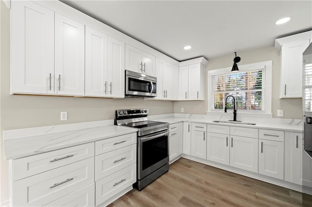 kitchen with white cabinetry, sink, stainless steel appliances, light stone countertops, and light wood-type flooring