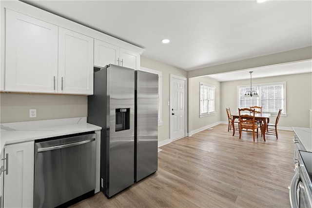 kitchen featuring appliances with stainless steel finishes, white cabinets, hanging light fixtures, light stone counters, and light hardwood / wood-style flooring