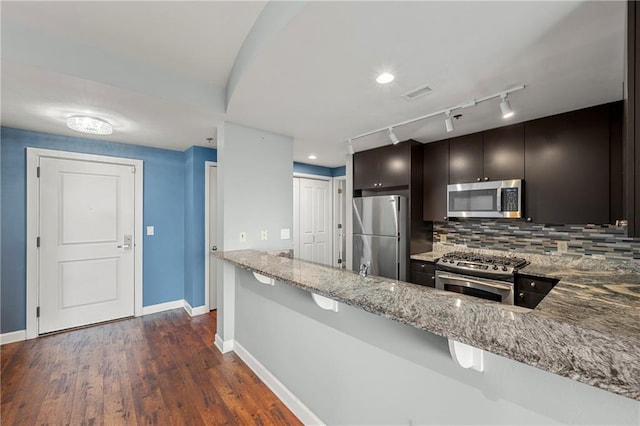 kitchen with light stone counters, stainless steel appliances, tasteful backsplash, dark wood-type flooring, and kitchen peninsula