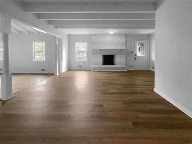 unfurnished living room featuring dark wood-type flooring, a brick fireplace, and beamed ceiling