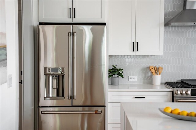 kitchen with appliances with stainless steel finishes, decorative backsplash, white cabinetry, and wall chimney range hood