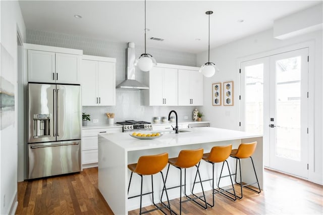 kitchen featuring decorative light fixtures, a kitchen island with sink, appliances with stainless steel finishes, and wall chimney exhaust hood