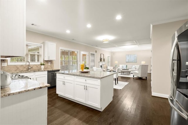 kitchen with light stone counters, a kitchen island, white cabinets, open floor plan, and appliances with stainless steel finishes