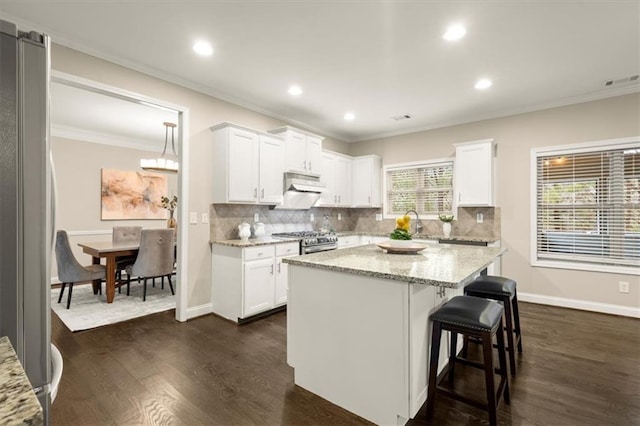 kitchen with light stone countertops, stainless steel appliances, dark wood-style flooring, white cabinets, and a center island