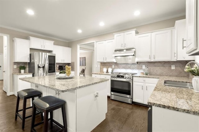 kitchen featuring under cabinet range hood, stainless steel appliances, a sink, a kitchen island, and white cabinetry