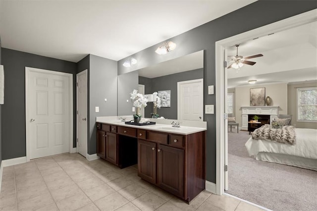 bathroom featuring a fireplace, double vanity, ceiling fan, a sink, and baseboards