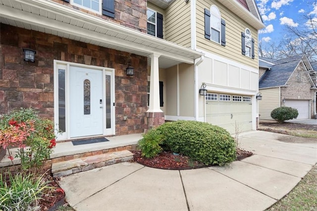 entrance to property featuring driveway, stone siding, a garage, and board and batten siding