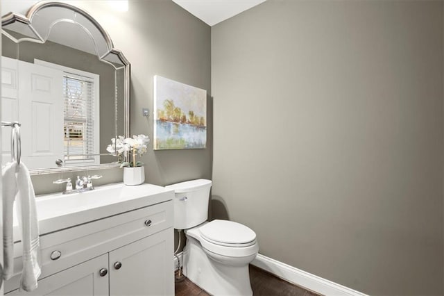 half bath featuring baseboards, vanity, toilet, and wood finished floors