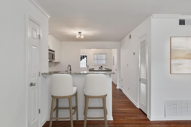 kitchen featuring dark wood-type flooring, a kitchen bar, white cabinetry, kitchen peninsula, and light stone countertops