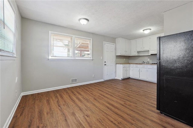 kitchen featuring black fridge, white cabinetry, a textured ceiling, and dark hardwood / wood-style flooring