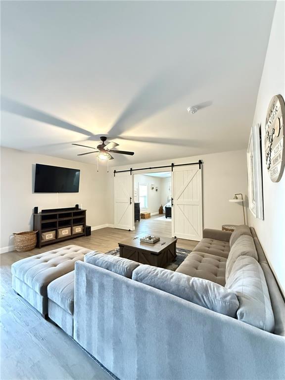 living room with hardwood / wood-style flooring, a barn door, and ceiling fan