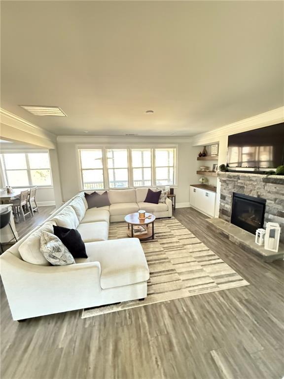 living room featuring hardwood / wood-style flooring, ornamental molding, a stone fireplace, and a healthy amount of sunlight