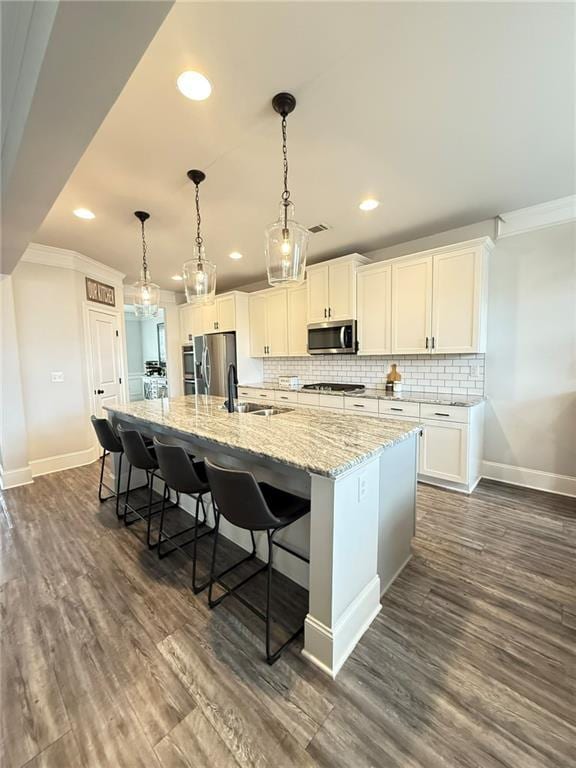 kitchen featuring white cabinetry, light stone counters, decorative light fixtures, appliances with stainless steel finishes, and an island with sink