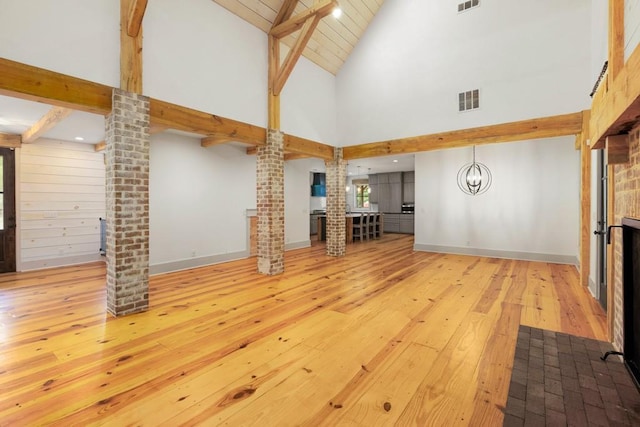 unfurnished living room featuring hardwood / wood-style floors, high vaulted ceiling, beamed ceiling, a chandelier, and ornate columns