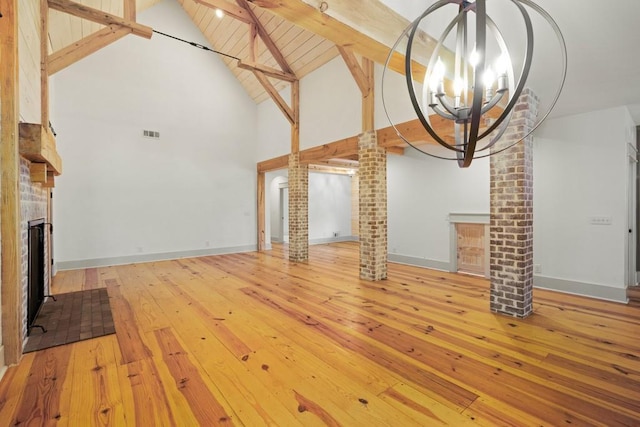 unfurnished living room featuring hardwood / wood-style floors, high vaulted ceiling, decorative columns, a notable chandelier, and beamed ceiling