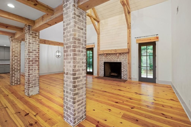 unfurnished living room with ornate columns, hardwood / wood-style floors, high vaulted ceiling, a fireplace, and beamed ceiling