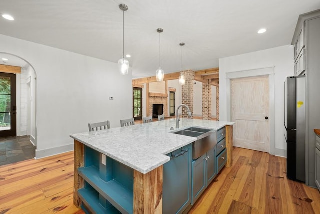 kitchen with pendant lighting, a fireplace, sink, a center island with sink, and light hardwood / wood-style flooring