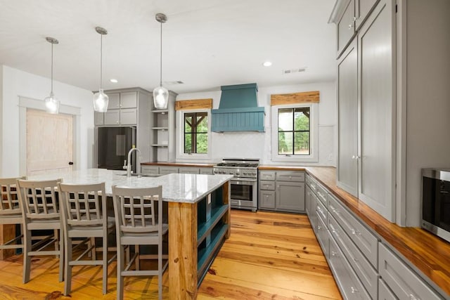 kitchen with premium range hood, gray cabinetry, light stone counters, decorative light fixtures, and stainless steel appliances