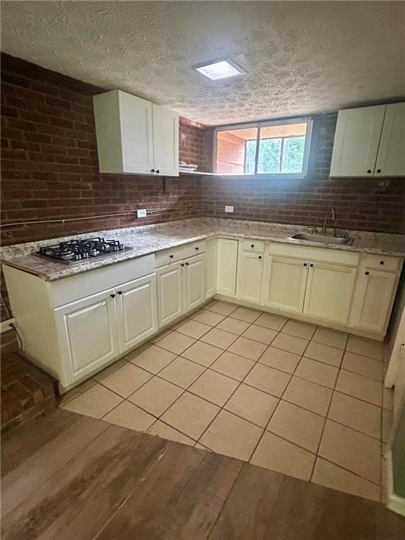 6072 Holiday Blvd, Forest Park, GA 30265 - kitchen with stainless steel gas stovetop, a sink, light wood finished floors, a textured ceiling, and white cabinetry