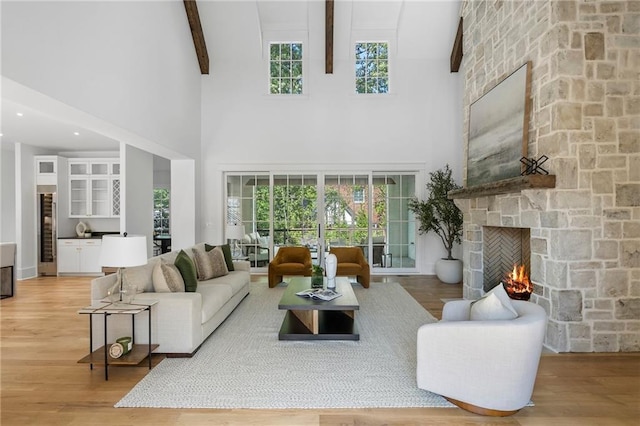 living room featuring beamed ceiling, a stone fireplace, a towering ceiling, and wood-type flooring