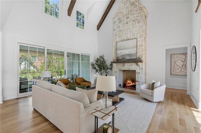 living room with beamed ceiling, light hardwood / wood-style floors, a fireplace, and a high ceiling